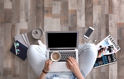 Young man with laptop and cup of coffee sitting on floor, top view