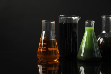 Photo of Glass flasks and beaker with different types of oil on black background