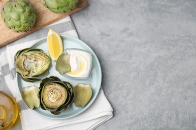 Delicious cooked artichokes with tasty sauce served on grey table, flat lay. Space for text