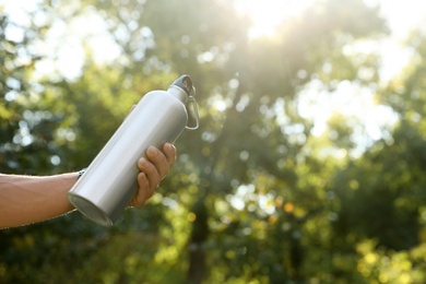 Photo of Young man holding bottle of water in park on sunny day, closeup. Space for text