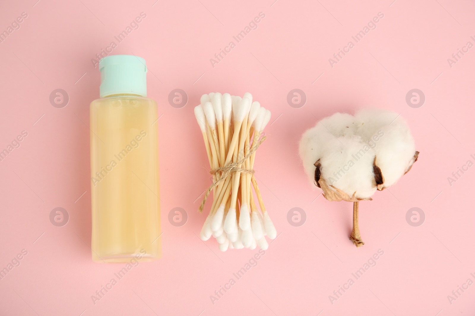 Photo of Bottle of cosmetic product, cotton buds and flower on pink background, flat lay