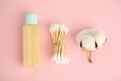 Photo of Bottle of cosmetic product, cotton buds and flower on pink background, flat lay