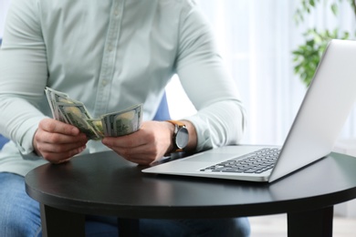 Photo of Businessman with laptop and money at table indoors, closeup