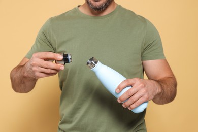 Photo of Man opening thermo bottle on beige background, closeup
