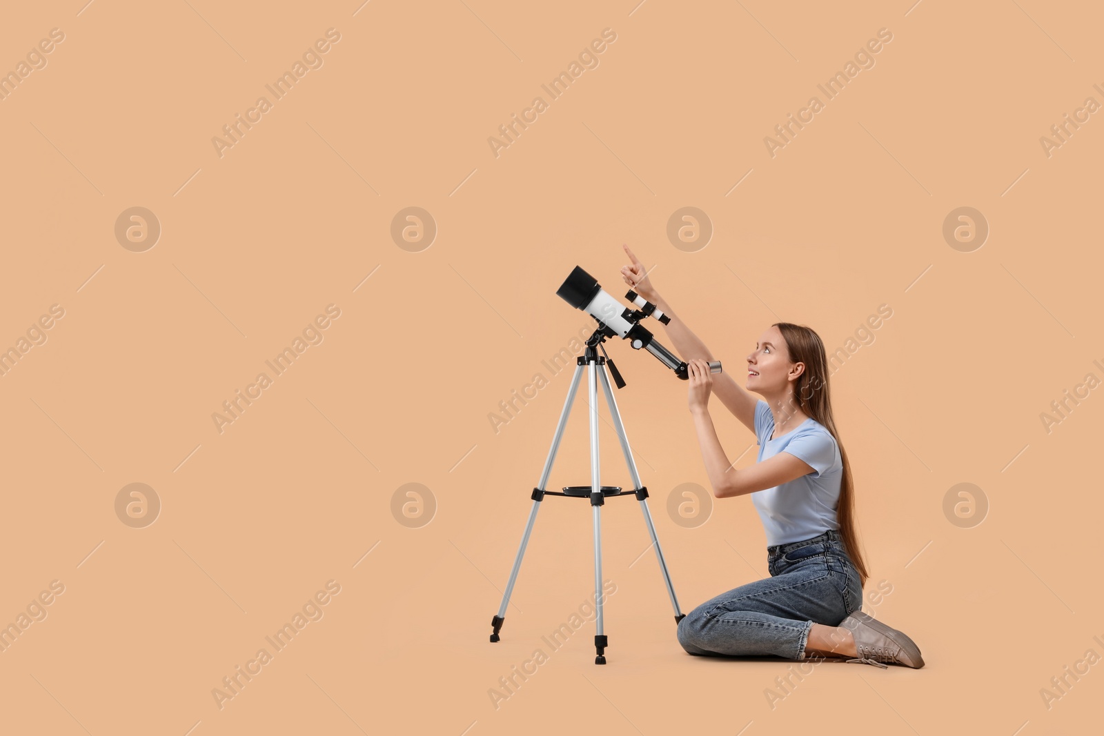 Photo of Young astronomer with telescope pointing at something on beige background, space for text