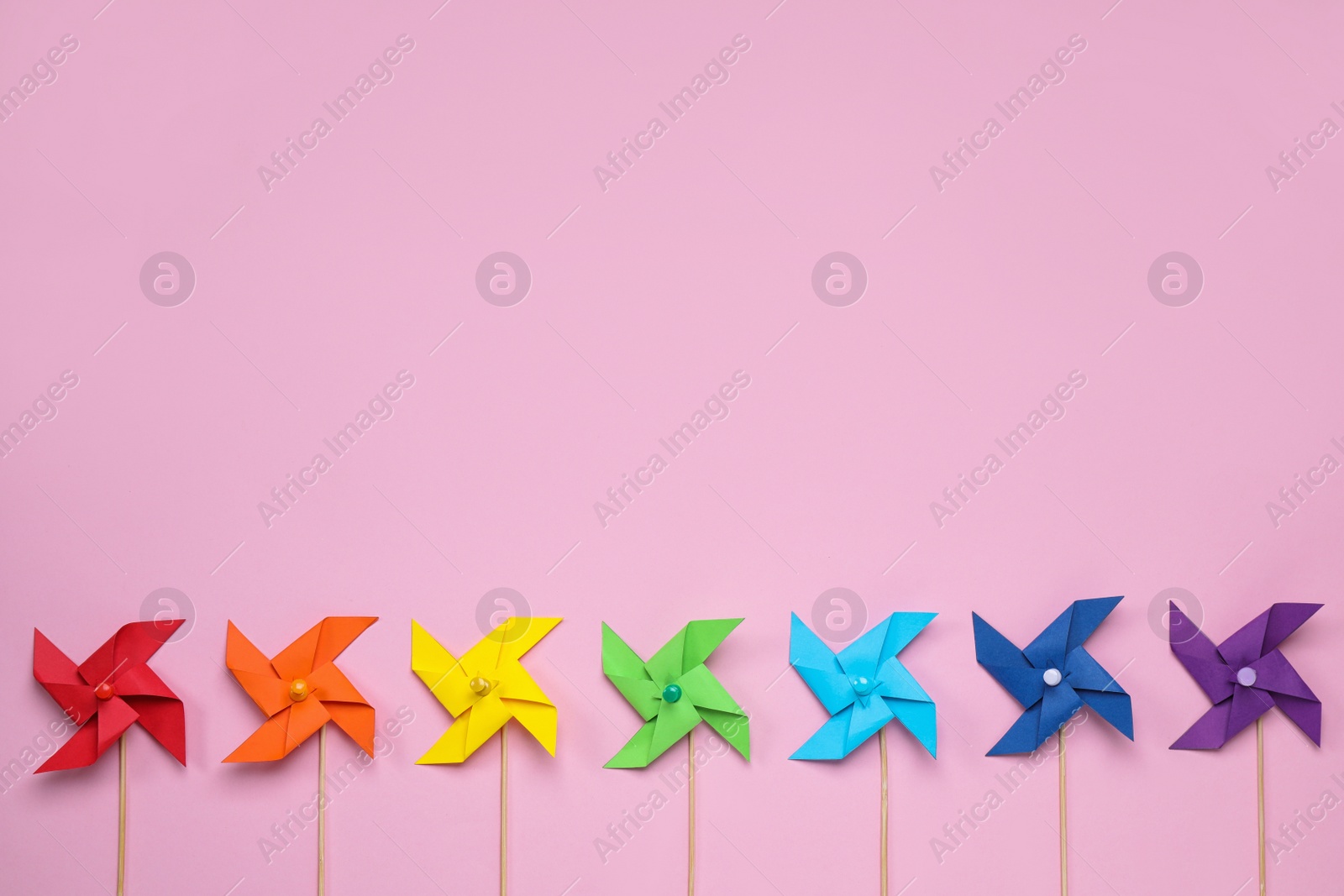 Photo of Colorful toy windmills on pink background, flat lay with space for text. Rainbow palette