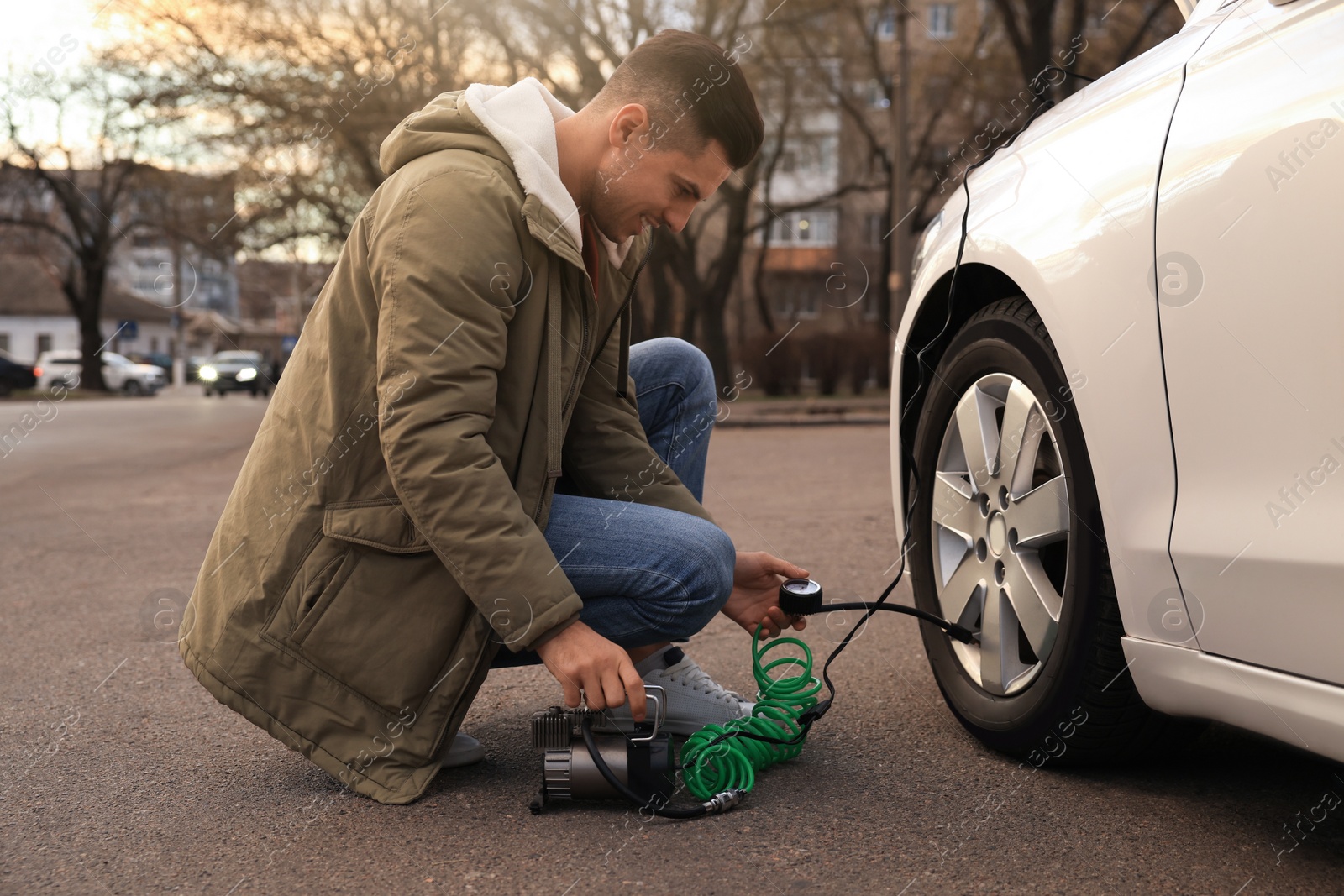 Photo of Handsome man inflating car tire with air compressor on street