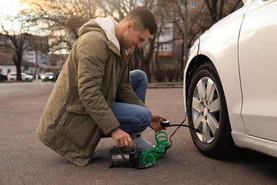 Photo of Handsome man inflating car tire with air compressor on street