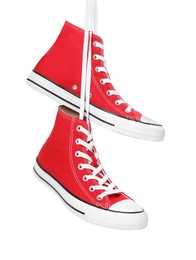 Photo of Pair of new red stylish high top plimsolls hanging on white background