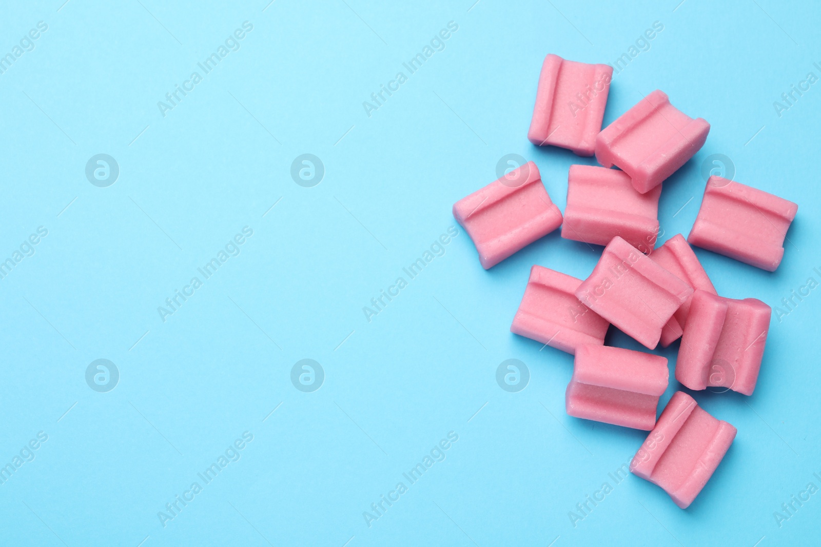 Photo of Tasty pink chewing gums on light blue background, flat lay. Space for text