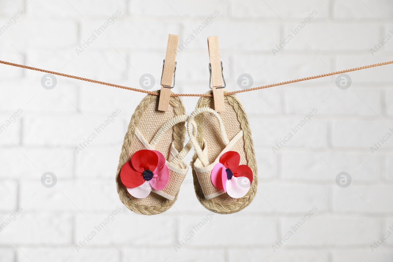 Photo of Cute baby shoes drying on washing line against white brick wall