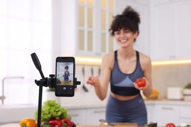 Photo of Food blogger cooking while recording video in kitchen, focus on smartphone