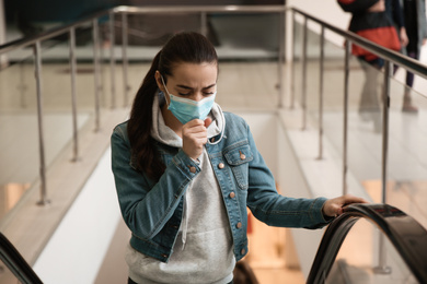 Photo of Young woman with disposable mask on escalator in mall. Dangerous virus