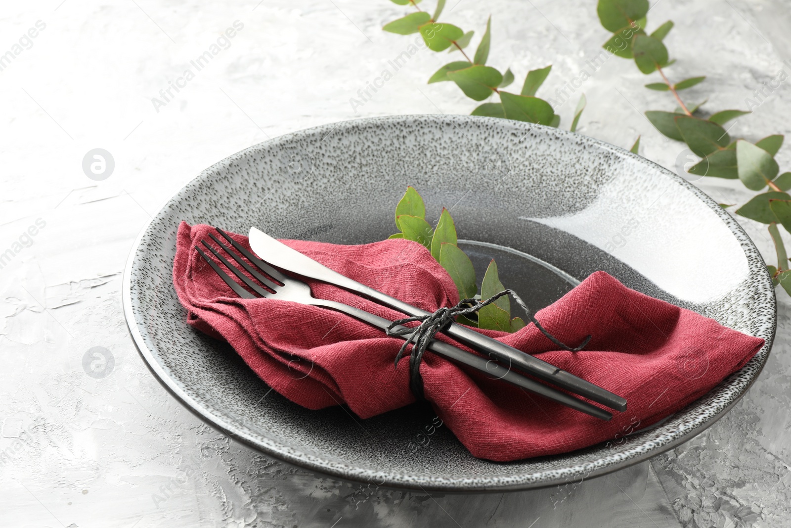 Photo of Stylish setting with cutlery, napkin, eucalyptus branches and plate on grey textured table, closeup