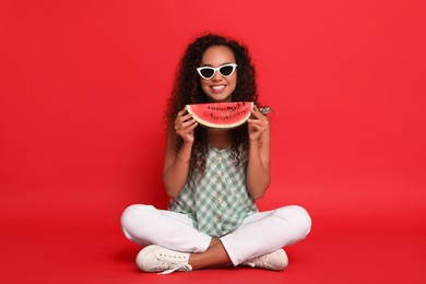 Photo of Beautiful young African American woman with slice of watermelon on red background