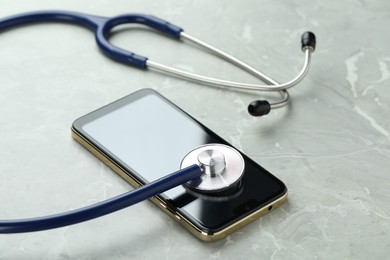 Modern smartphone and stethoscope on grey table