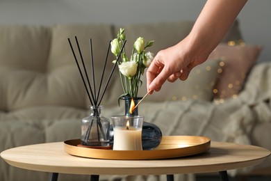 Photo of Woman lighting candle at wooden table in living room, closeup