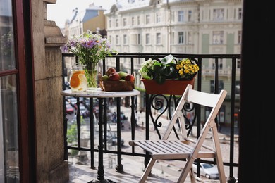 Photo of Relaxing atmosphere. Refreshing drink, apples and beautiful flowers on table near potted houseplants at balcony