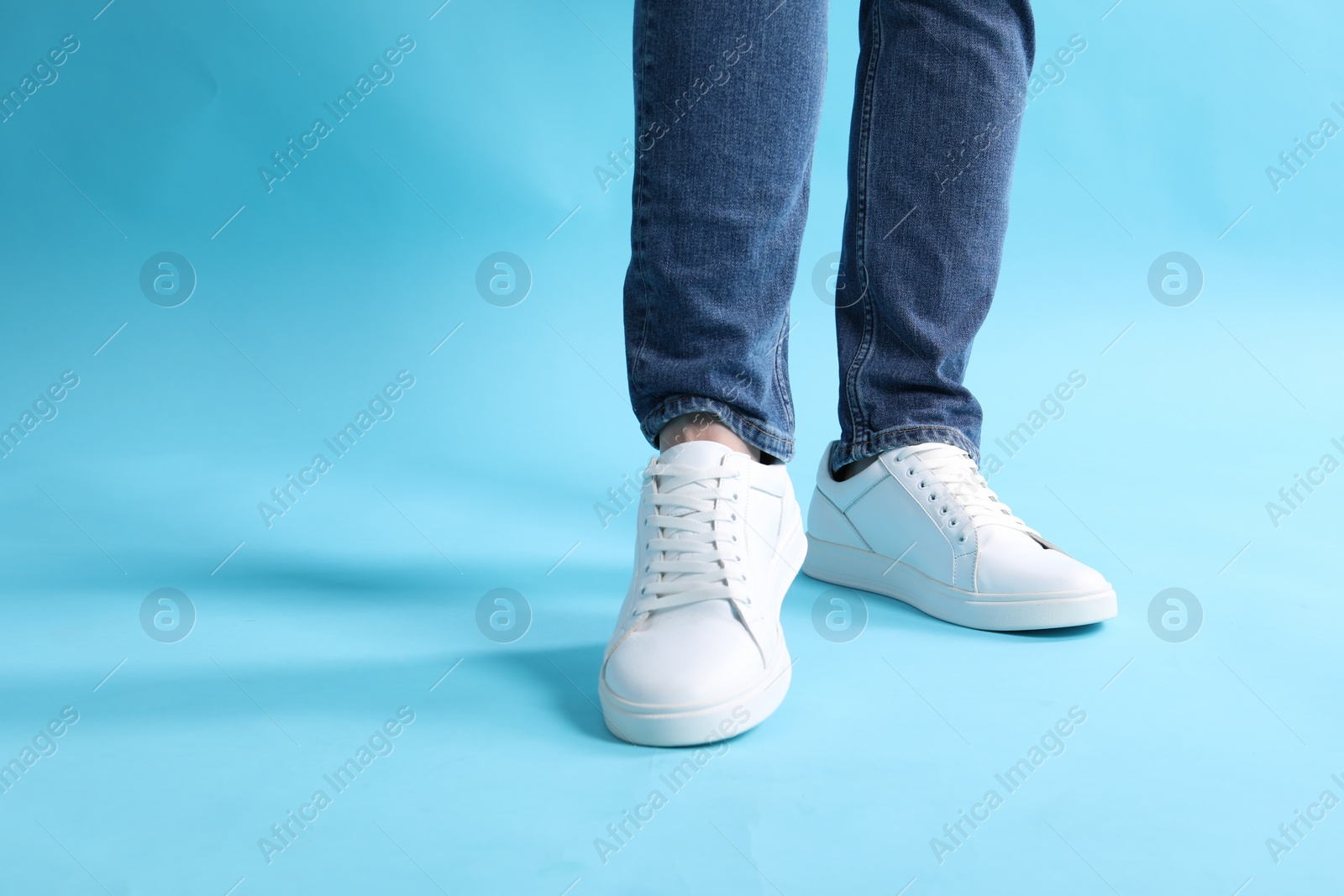 Photo of Man wearing stylish white sneakers on light blue background, closeup