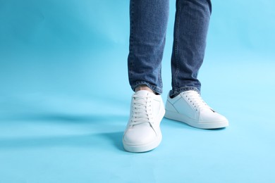 Man wearing stylish white sneakers on light blue background, closeup