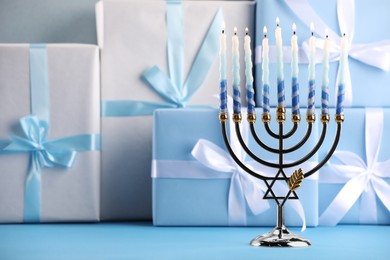Hanukkah celebration. Menorah with burning candles and gift boxes on light blue table, space for text