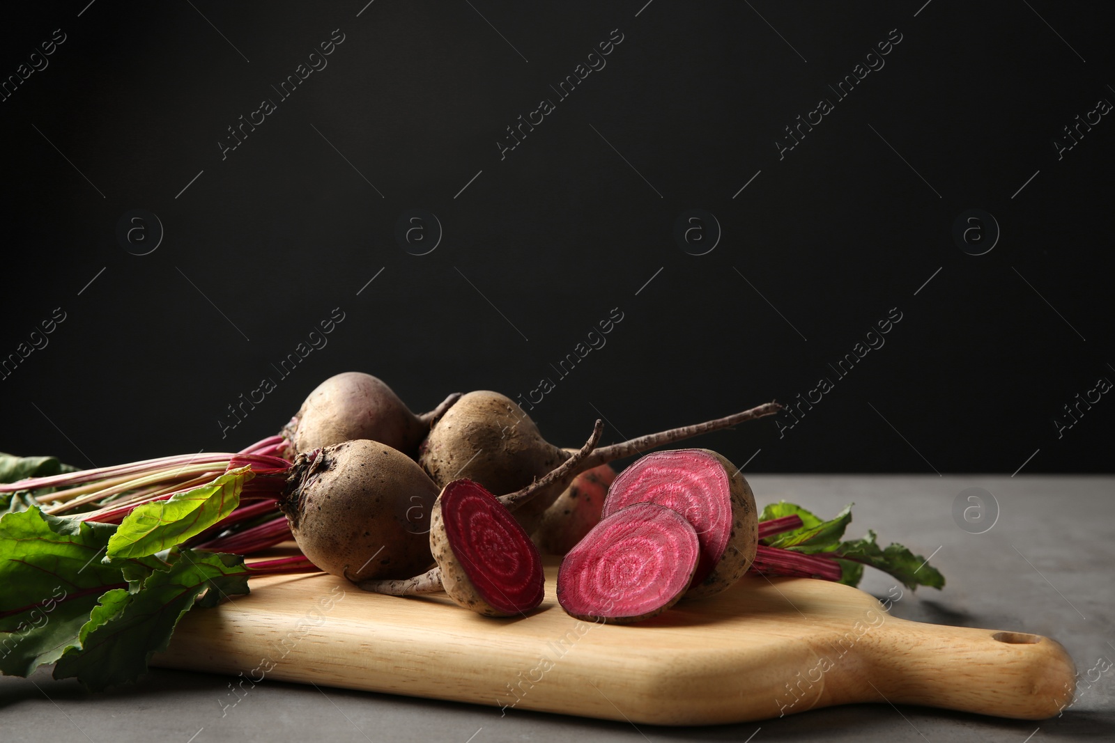 Photo of Wooden board with fresh beets on grey table against black background. Space for text