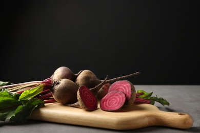 Wooden board with fresh beets on grey table against black background. Space for text