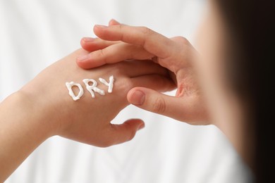 Photo of Young woman with word Dry made of cream on her hand on bed, closeup