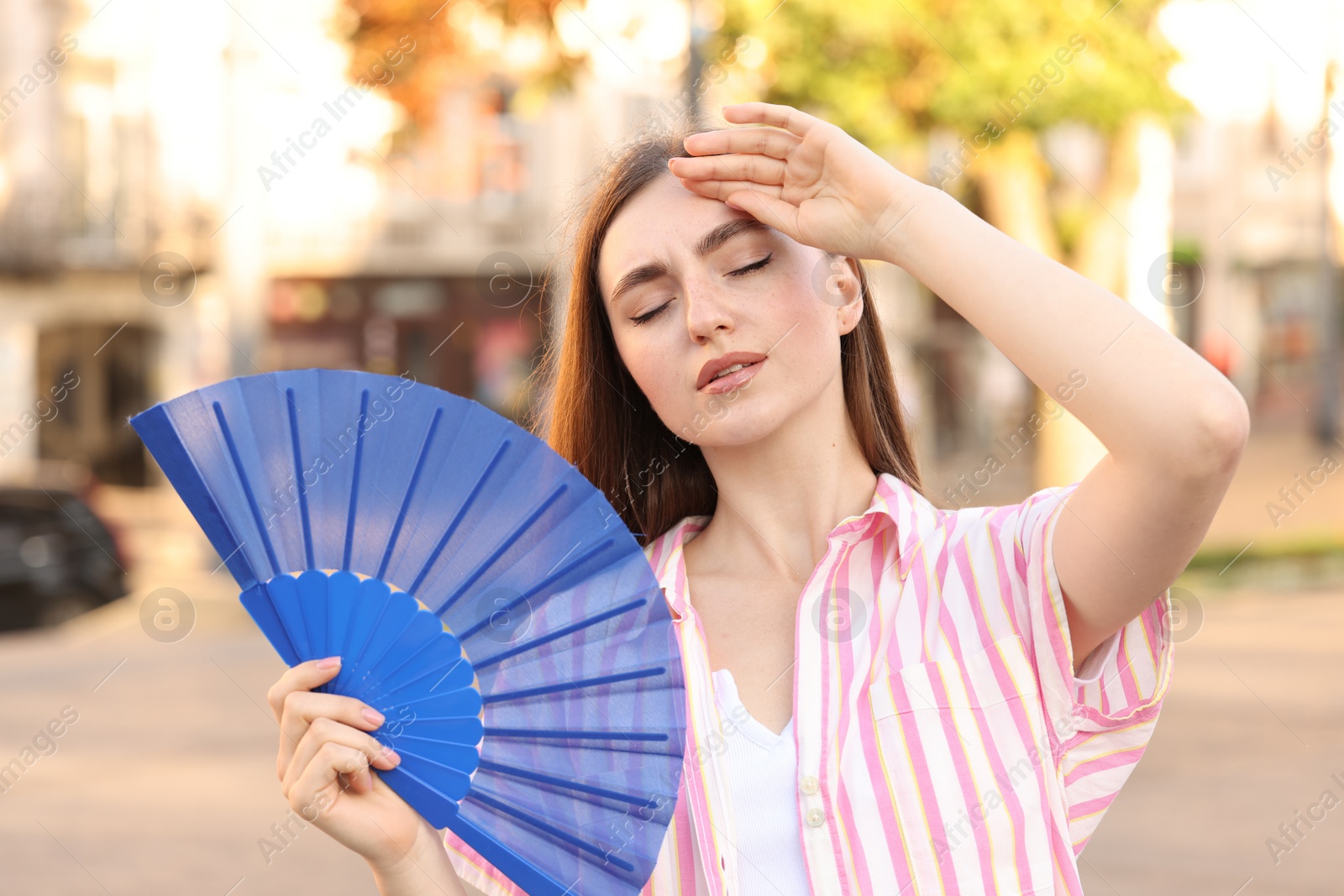 Photo of Woman with hand fan suffering from heat outdoors