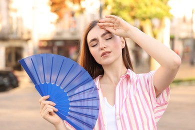 Woman with hand fan suffering from heat outdoors