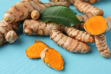 Photo of Whole and cut turmeric roots on light blue wooden table, closeup