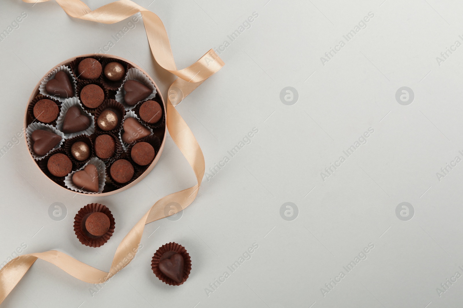 Photo of Different delicious chocolate candies in box and ribbon on light background, flat lay. Space for text