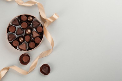 Different delicious chocolate candies in box and ribbon on light background, flat lay. Space for text