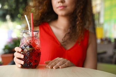 Photo of African-American woman with glass of natural lemonade in cafe, closeup. Detox drink