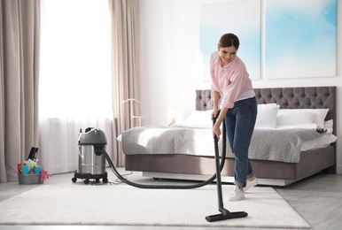 Woman removing dirt from carpet with vacuum cleaner at home