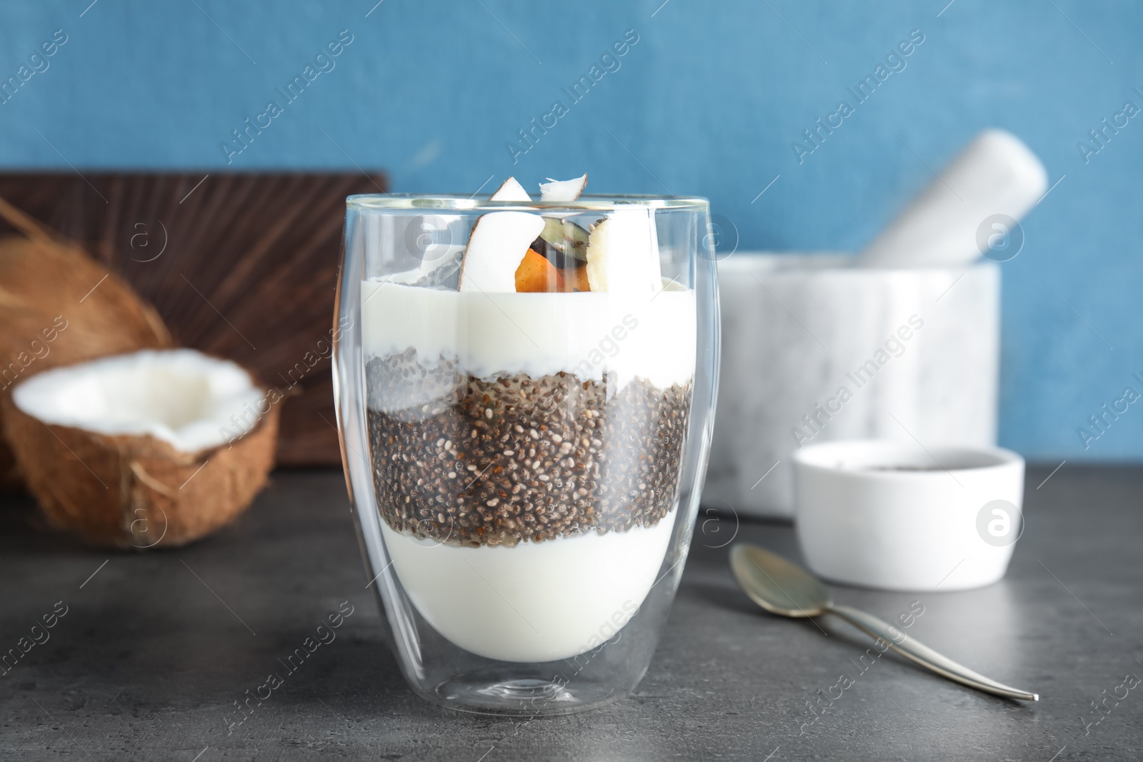 Photo of Glass of tasty chia seed pudding with coconut and ingredients on table