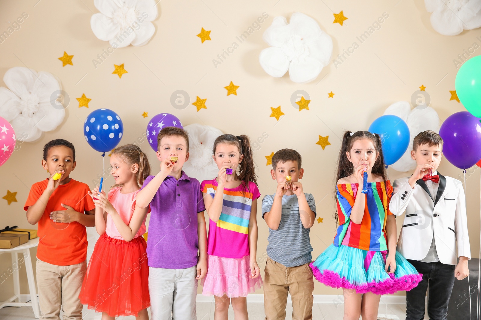 Photo of Adorable children with party blowers indoors. Birthday celebration