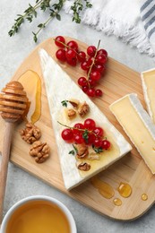 Photo of Brie cheese served with red currants, walnuts and honey on light table, flat lay