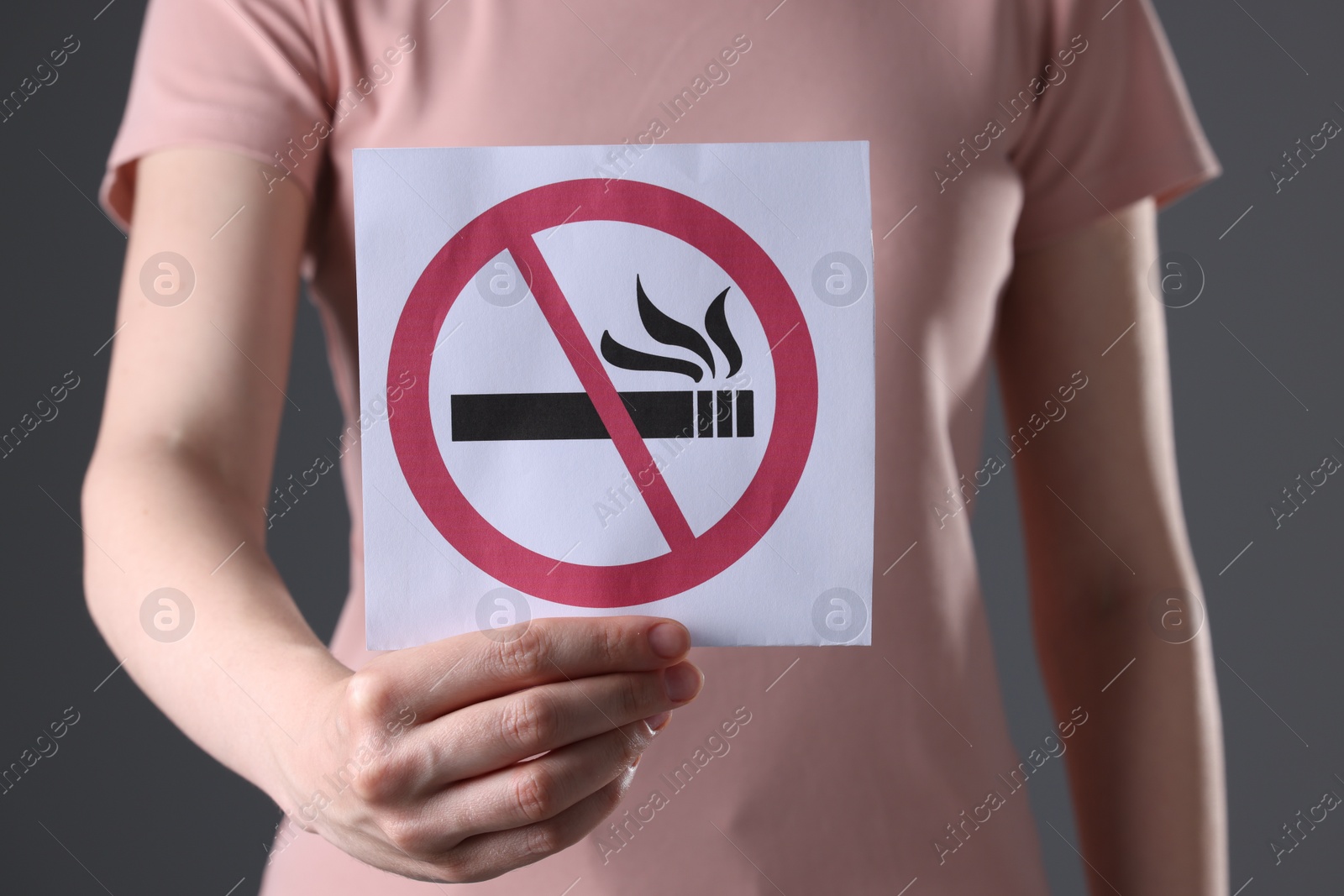 Photo of Woman holding card with no smoking sign on gray background, closeup