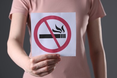 Photo of Woman holding card with no smoking sign on gray background, closeup