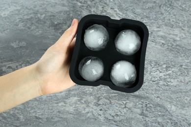 Woman holding mold with frozen ice balls at grey table, top view