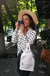 Beautiful young woman with stylish backpack and camera on city street