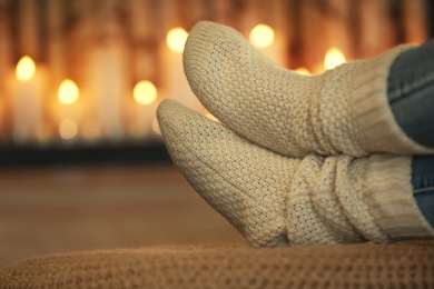 Photo of Woman wearing warm knitted socks near decorative fireplace indoors, closeup. Winter atmosphere