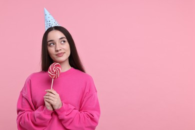 Woman in party hat holding lollipop on pink background