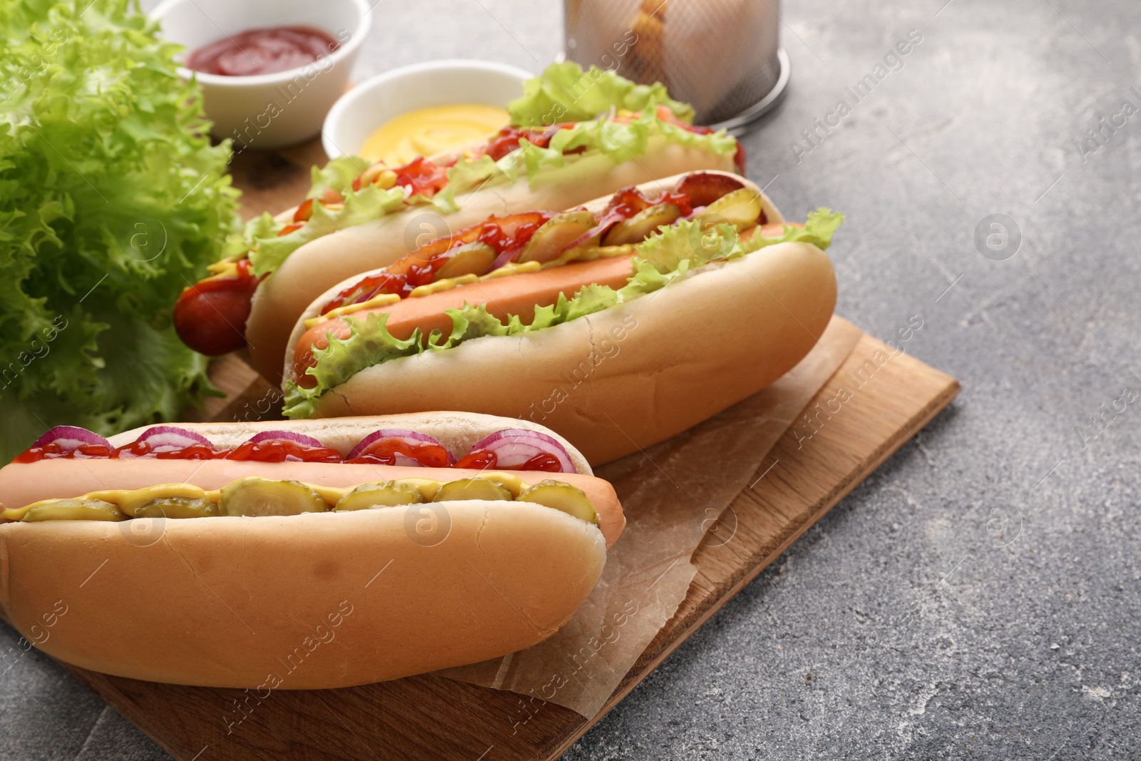 Photo of Delicious hot dogs with different toppings served on grey table. Space for text