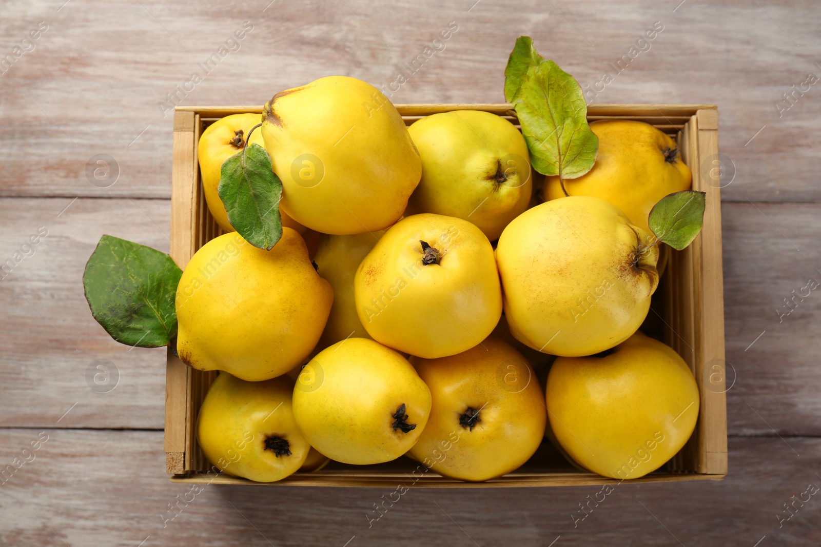 Photo of Tasty ripe quince fruits in crate on wooden table, top view