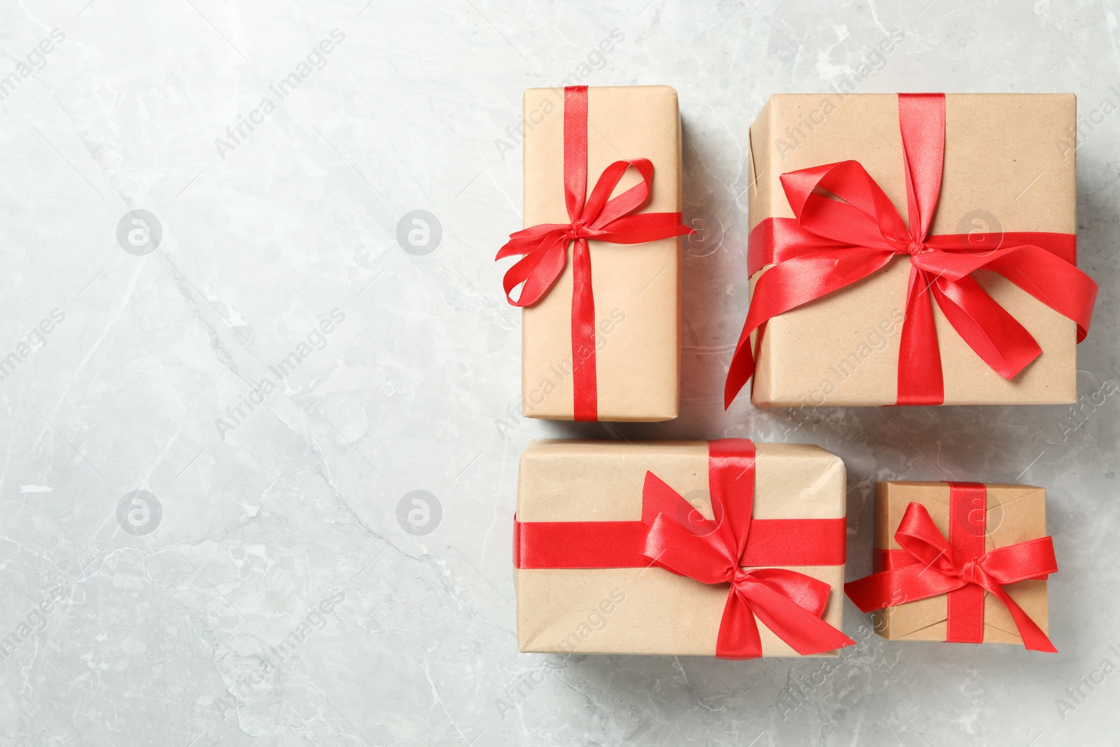 Photo of Christmas gift boxes with red bows on light grey marble background, flat lay. Space for text