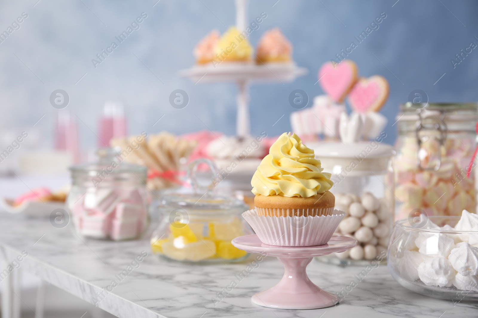 Photo of Stand with cupcake and other sweets on white marble table, space for text. Candy bar