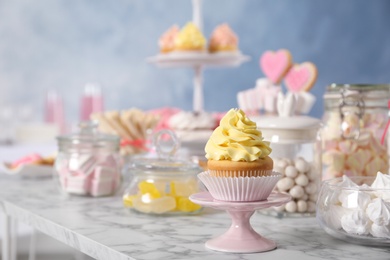 Photo of Stand with cupcake and other sweets on white marble table, space for text. Candy bar