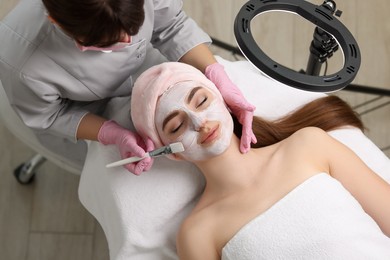 Photo of Cosmetologist applying mask on woman's face in clinic, top view